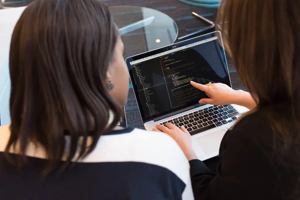 Dos mujeres revisan código juntas en una laptop